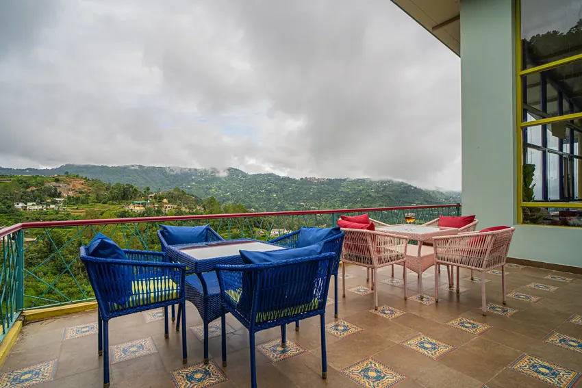 Balcony seating area with tables and chairs facing hills and cloudy sky